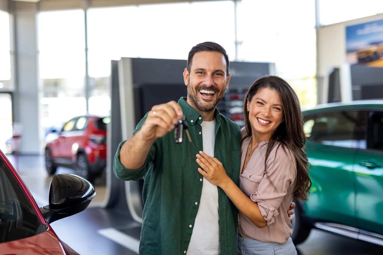 Casal sorrindo com as chaves do carro na concessionária
